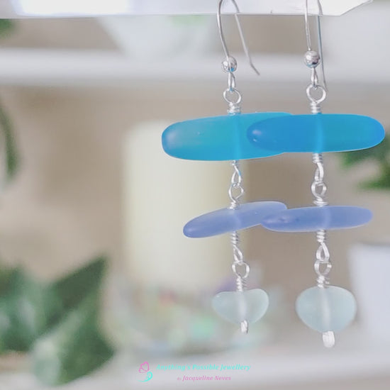  Long Silver Sea glass earrings with three different colors of blue glass from aqua to sky blue on french style earring hooks with plants in the background 