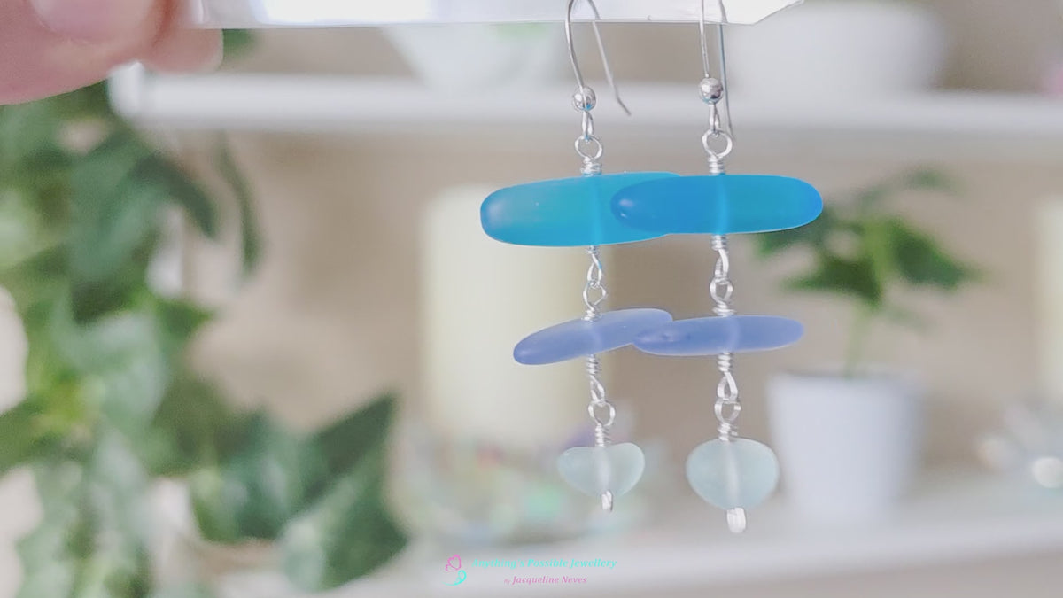  Long Silver Sea glass earrings with three different colors of blue glass from aqua to sky blue on french style earring hooks with plants in the background 