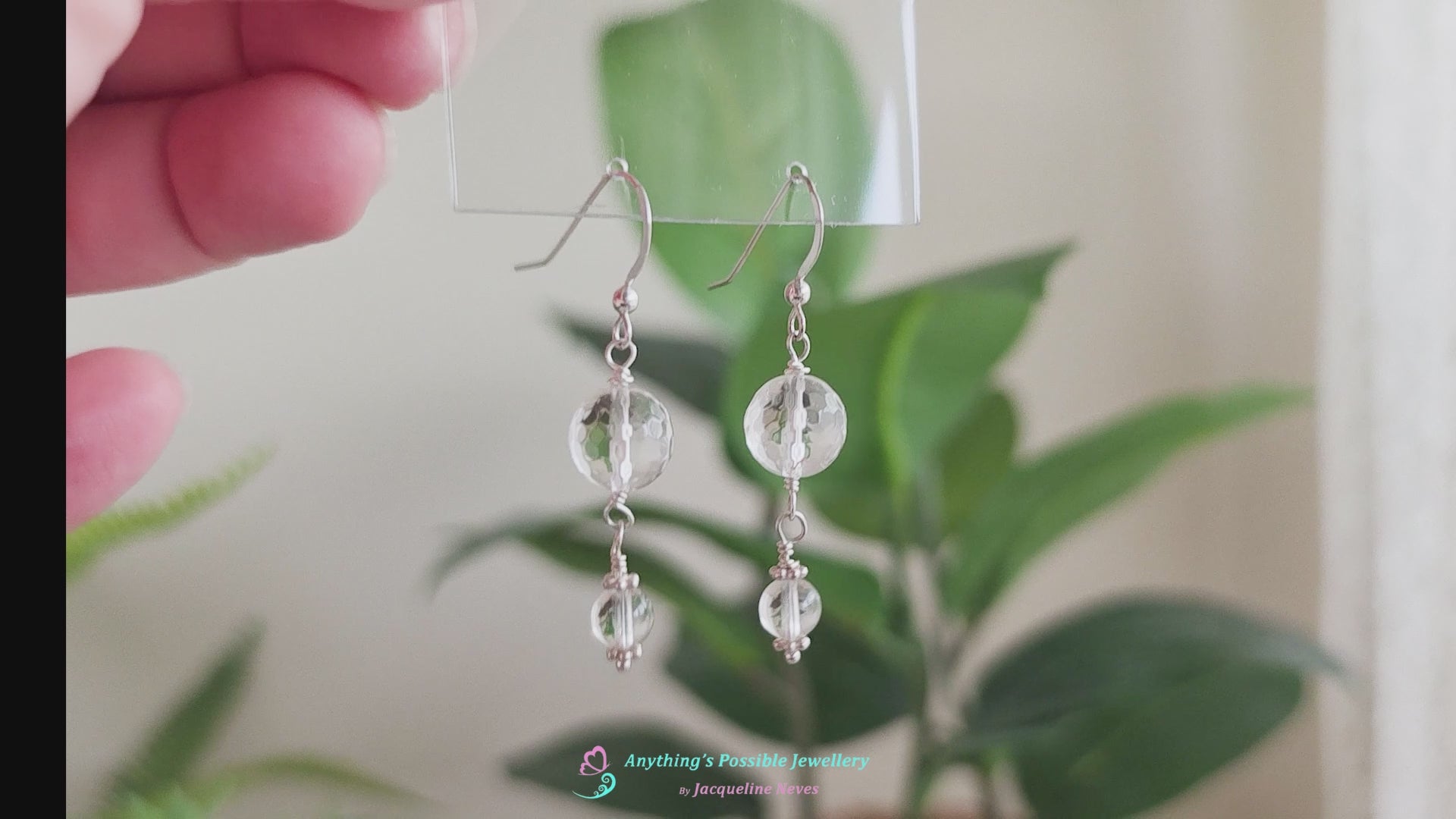Video of A pair of clear Quartz Crystal Earrings with faceted and polished stones with Sterling Silver beads, wire wrapped and french hooks hanging with plants in the background