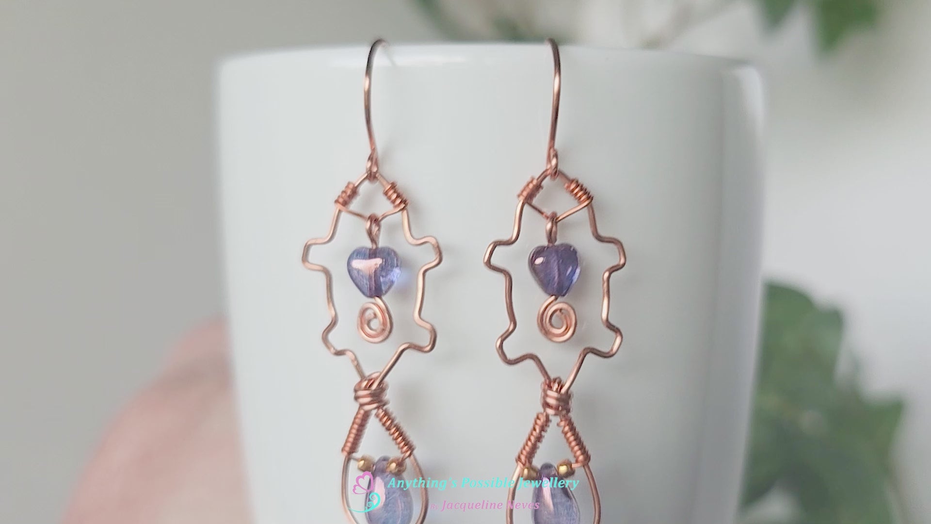 Video a pair of wire wrapped copper beaver earrings with mauve purple hearts and tear drop stones on white vase 