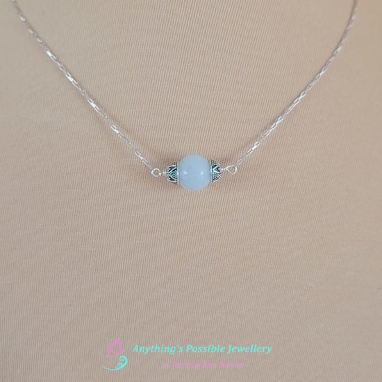 Video of handmade Aquamarine Necklace with one large single round blue Aquamarine stone with silver caps with elongated box chain on beige background display