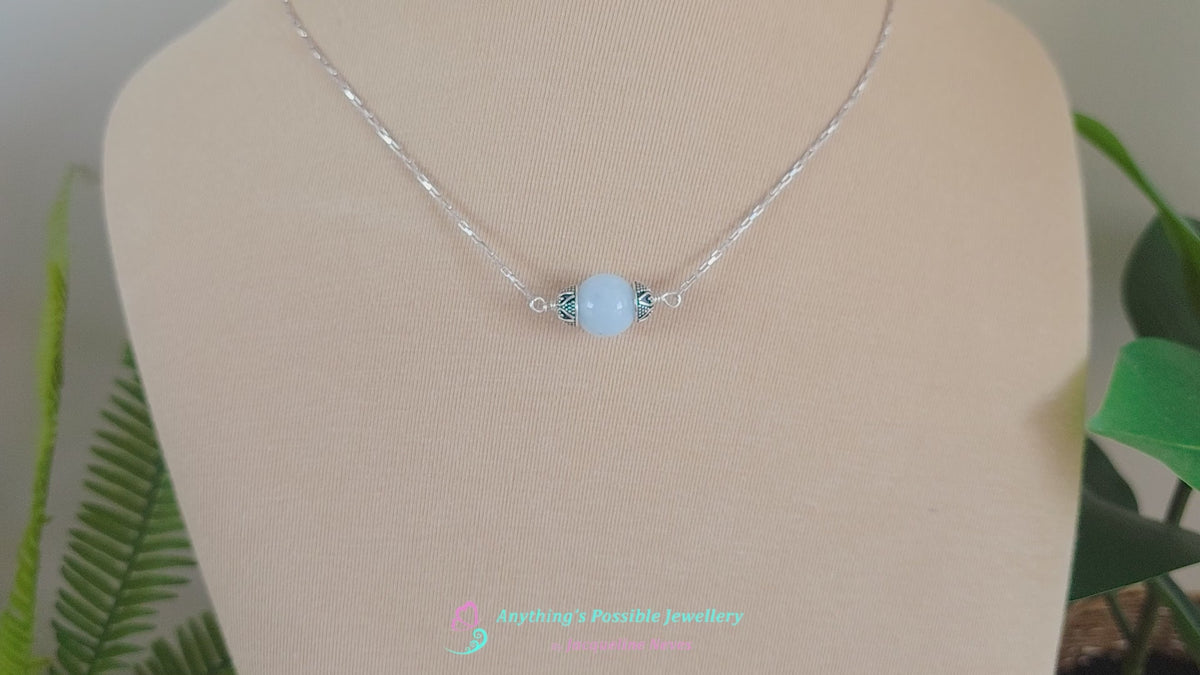 Video of handmade Aquamarine Necklace with one large single round blue Aquamarine stone with silver caps with elongated box chain on beige background display