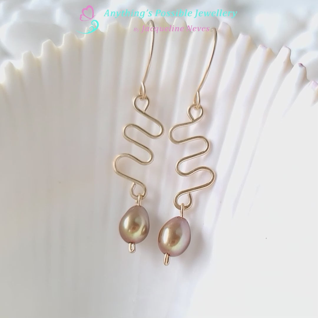 Video of a Long Gold Swirling, Wavy Design Earrings and drop shape gold Freshwater Cultured Pearls dangling from French style earring hooks, on white Background and shell