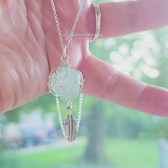 Video of Silver Pendant with Aqua Blue Sea Glass and dangling Silver Feather on Silver Rolo chain displayed in hand