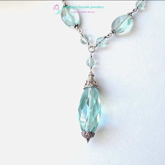 Art Deco style Aquamarine necklace made with large faceted, sparkly pale aqua blue translucent synthetic Aquamarine stones and Sterling Silver beads and chain on white background and plants 