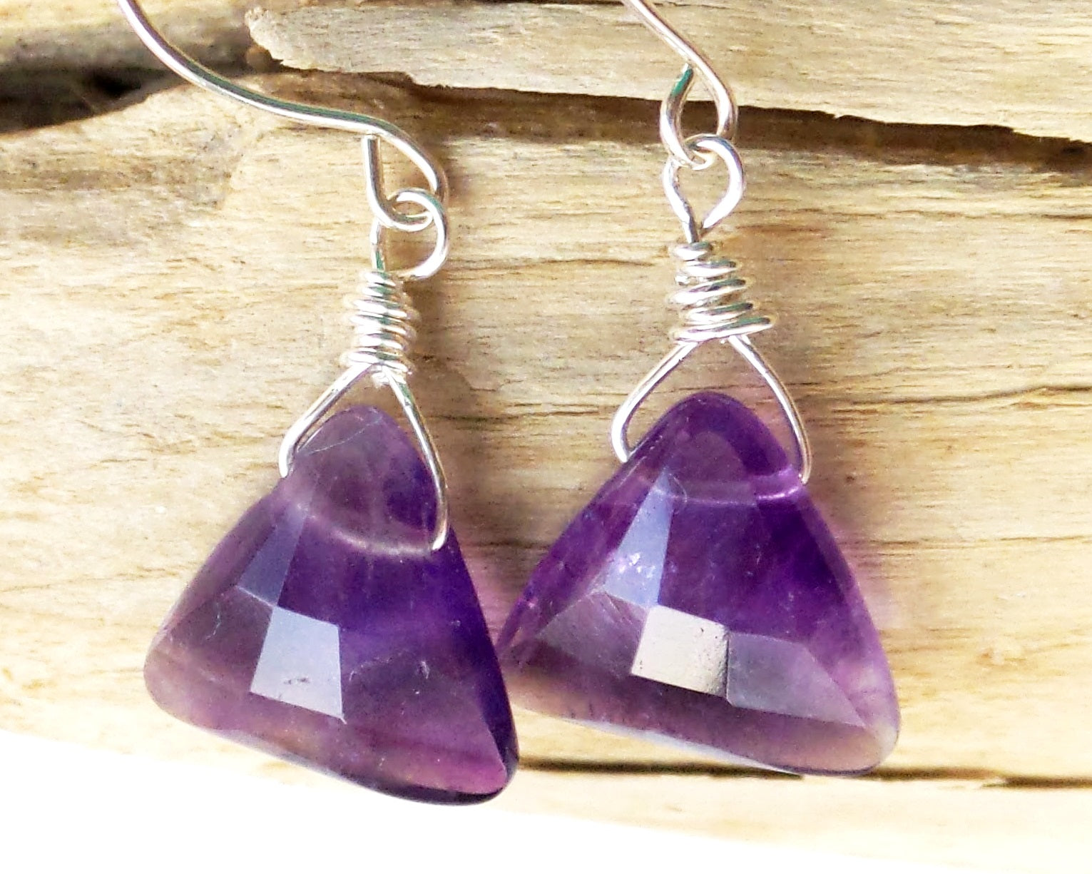 Genuine Amethyst Earrings made with solid 925 Sterling Silver and High quality triangle shaped, faceted, deep purple Gemstones, displayed on beach wood