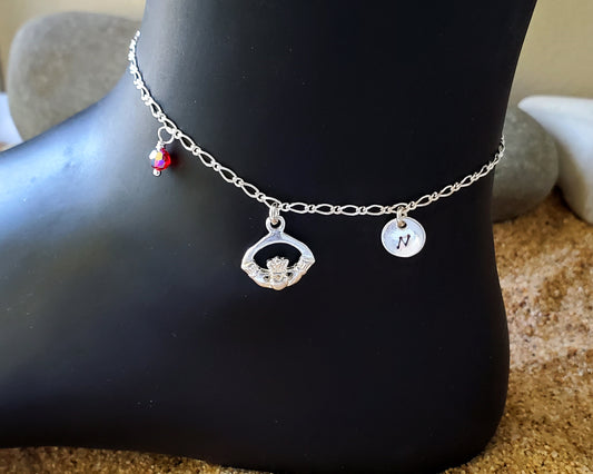 Personalized Claddagh Ankle Bracelet-Anklet with Initial and Crystal Birthstone pendants dangling from a flat figaro chain. 