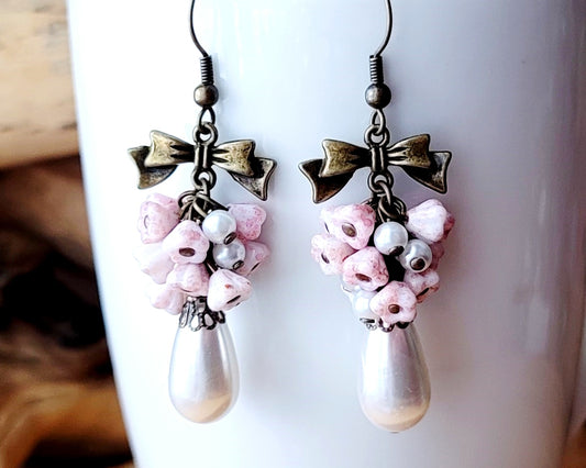 Vintage Romance White Pearl Pale Pink Flower Bow Earrings, Long Cluster earrings made with white Faux pearls and pale pink Czech flowers and Antiqued Brass finished metal.  Photo on White mug. 