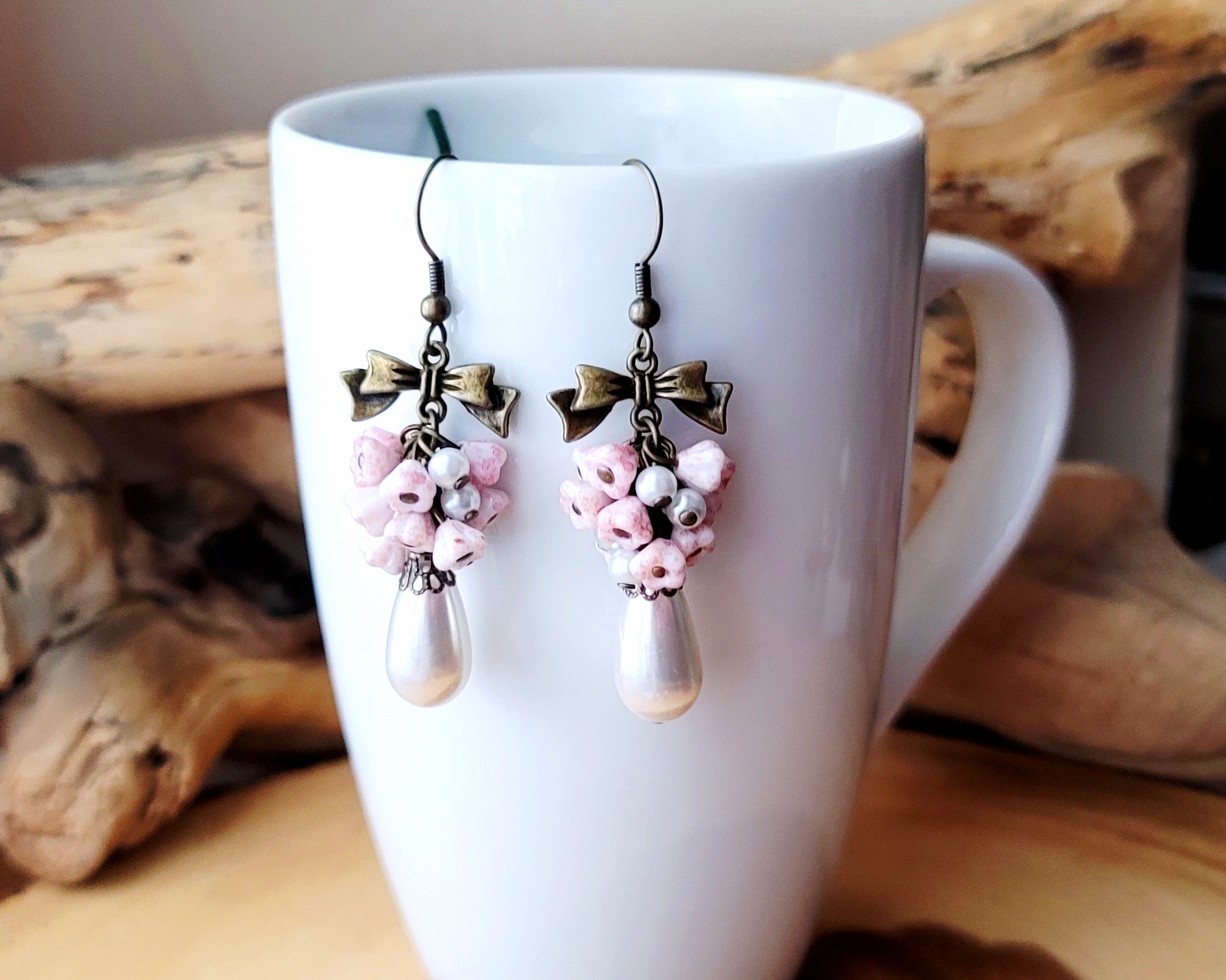 Vintage Romance White Pearl Pale Pink Flower Bow Earrings, Long Cluster earrings made with white Faux pearls and pale pink Czech flowers and Antiqued Brass finished metal.  Photo on White mug. 