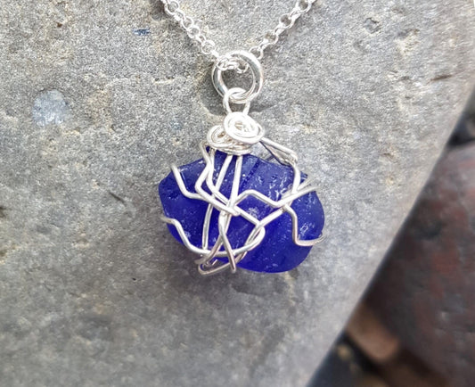 Sapphire Blue Passion Beach Glass Pendant Necklace, Sterling Silver wire wrapped blue beach glass pendant on rolo style chain. Displayed on grey rock.