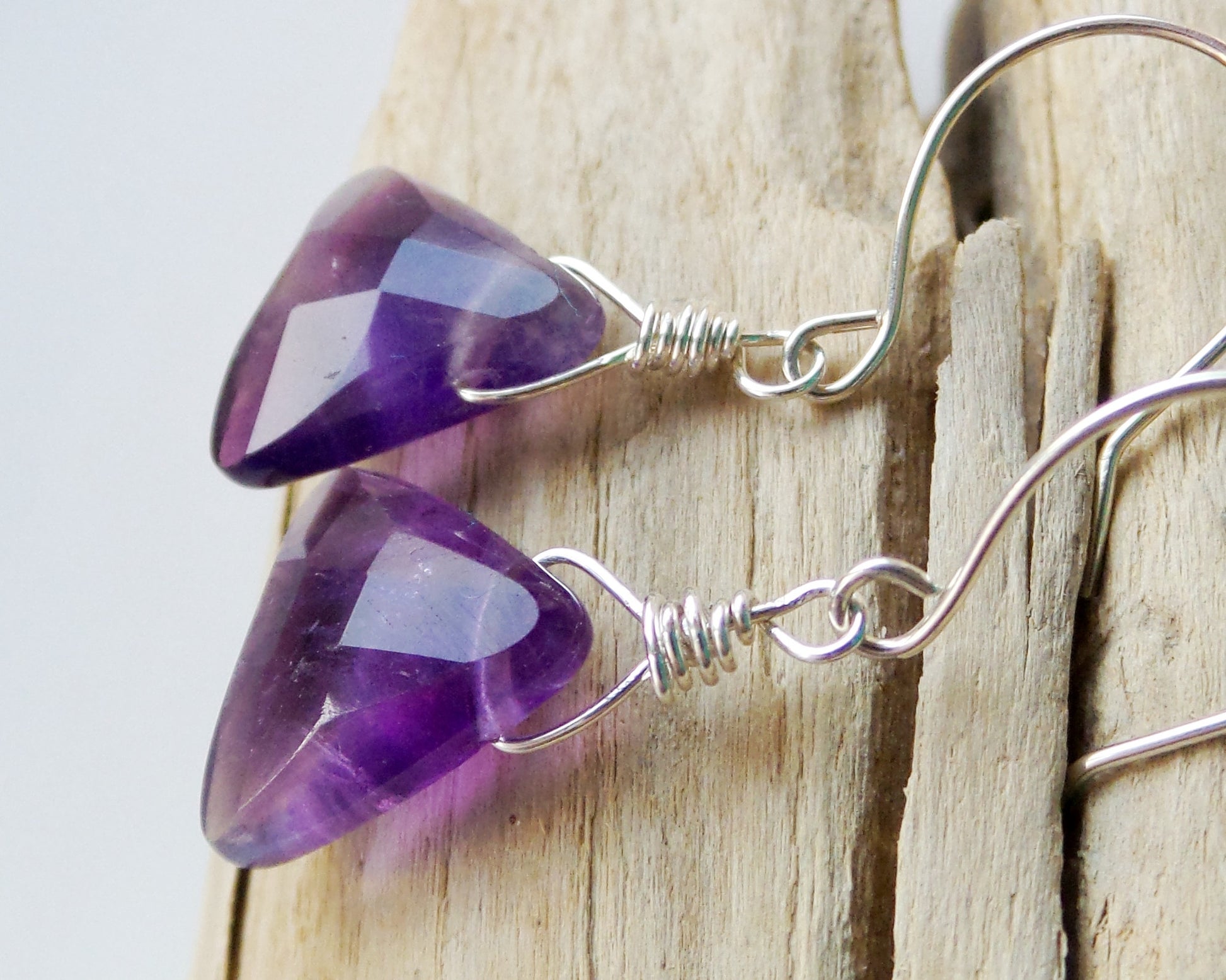 Genuine Amethyst Earrings made with solid 925 Sterling Silver and High quality triangle shaped, faceted, deep purple Gemstones, displayed on beach wood