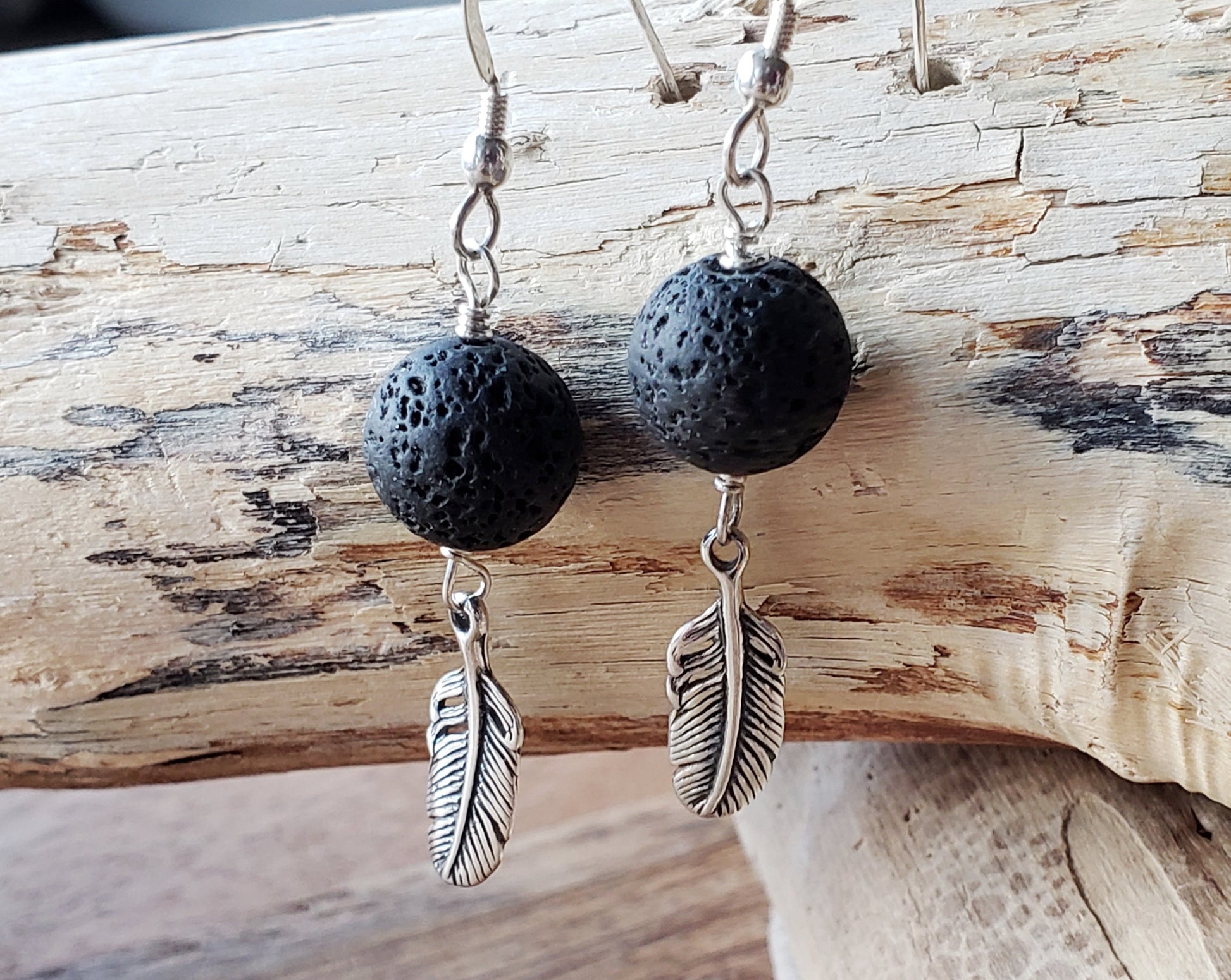 Long Feather Lava stone Earrings made with solid Sterling Silver Feather pendants and black Lava Stone on french earrings hooks displayed on beach wood 