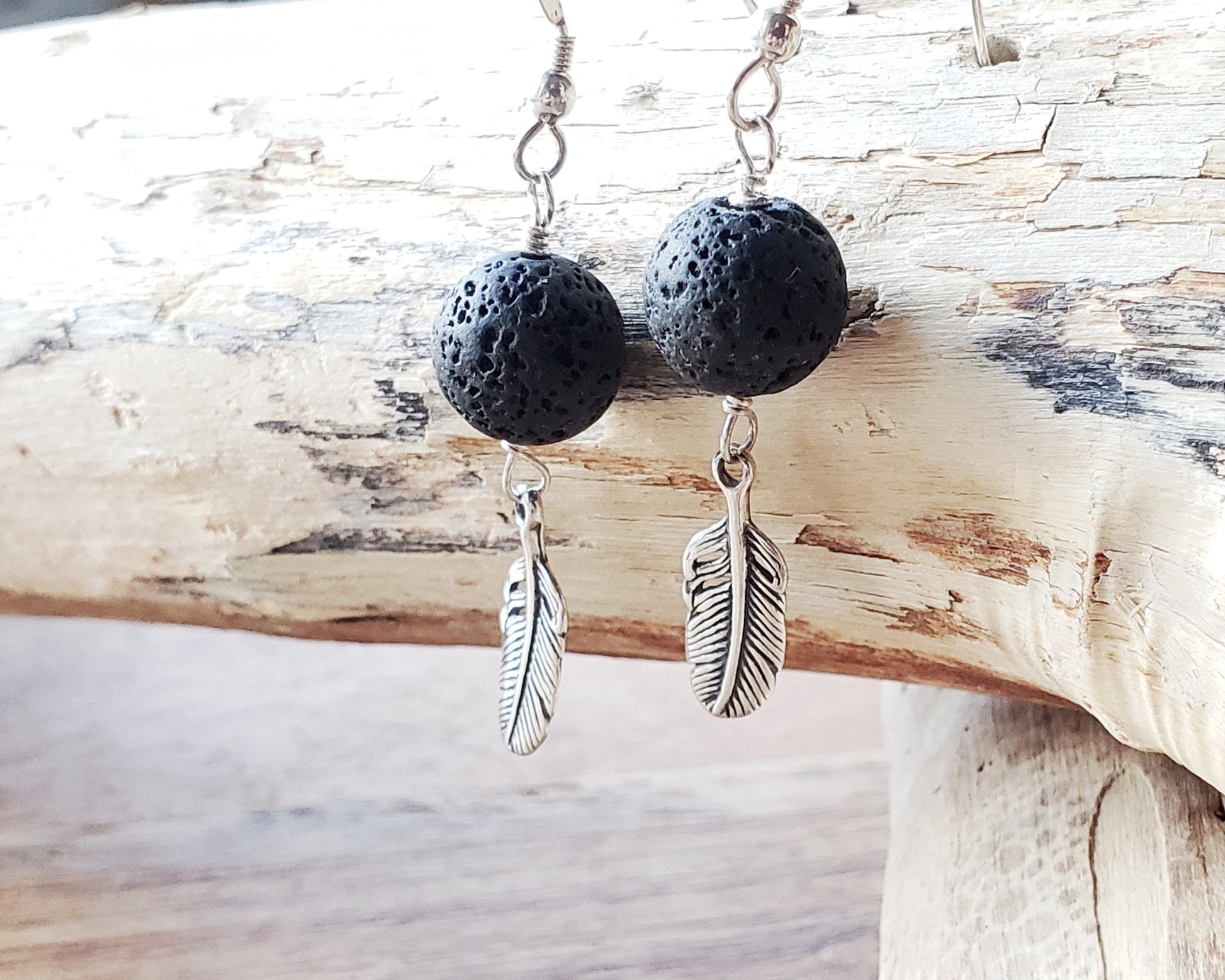 Long Feather Lava stone Earrings made with solid Sterling Silver Feather pendants and black Lava Stone on french earrings hooks displayed on beach wood 