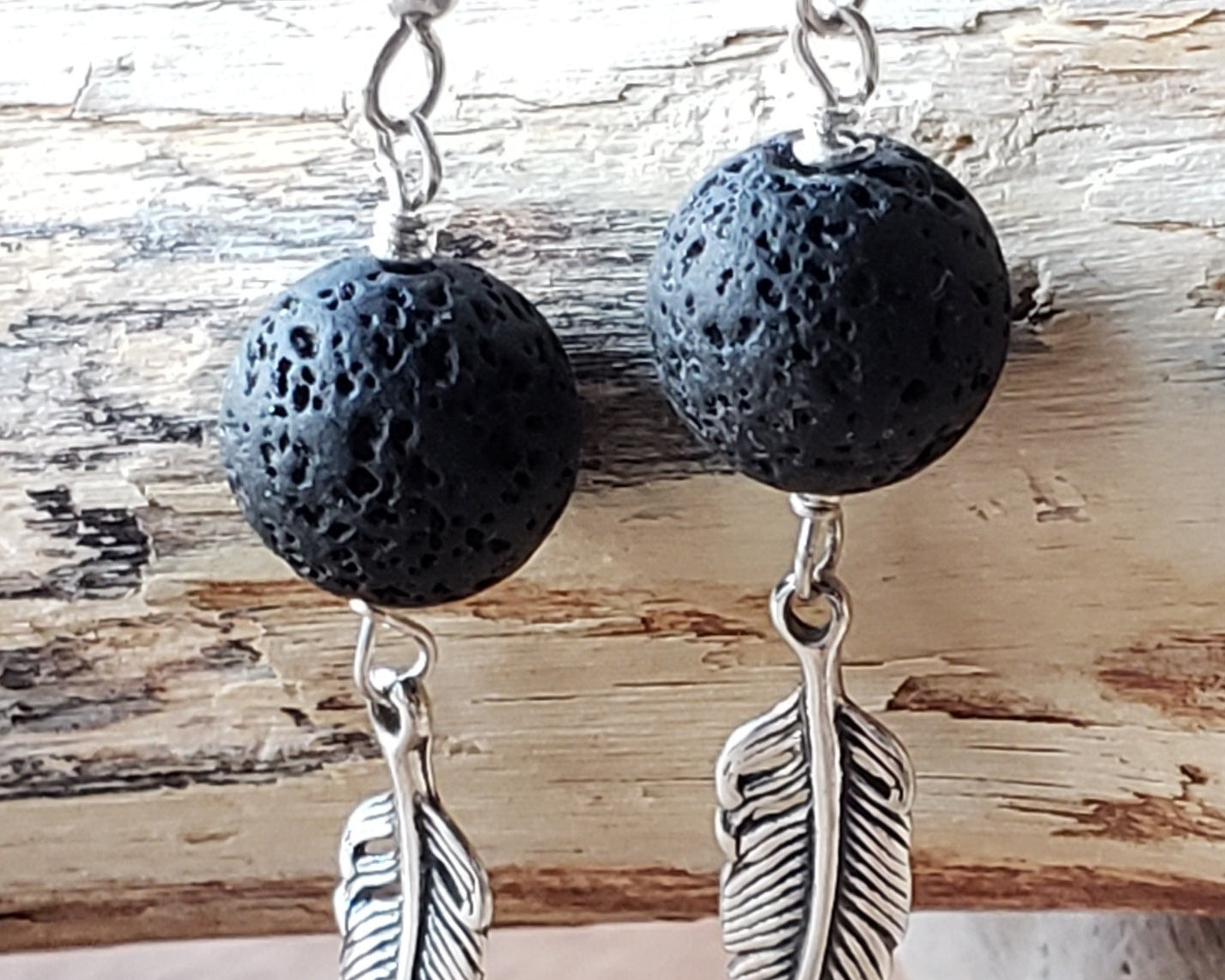 Long Feather Lava stone Earrings made with solid Sterling Silver Feather pendants and black Lava Stone on french earrings hooks displayed on beach wood 