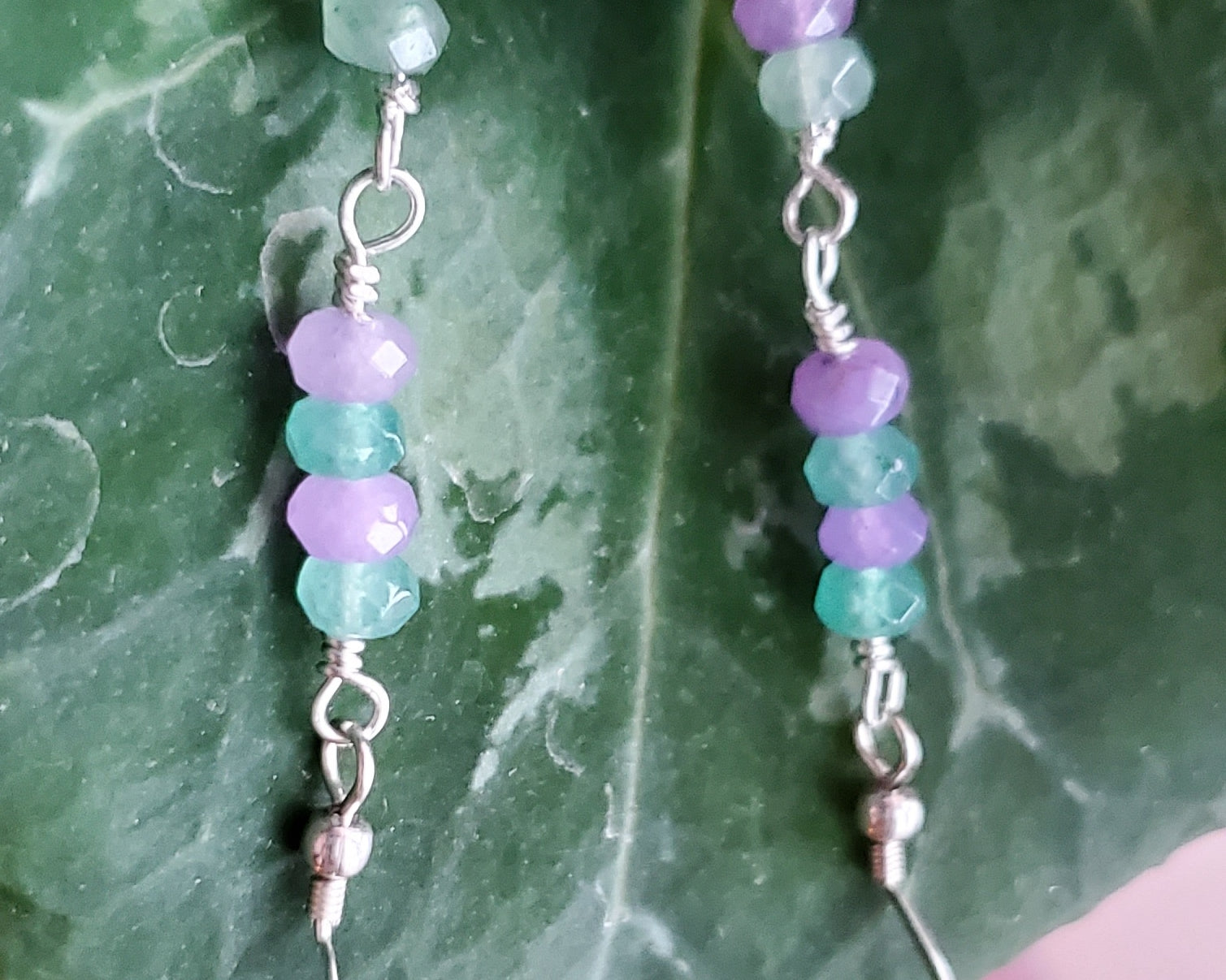 Long Lavender Flower Garden Earrings, Sterling Silver, Large round Floral Lampwork Glass beads with lavender purple and turquoise blue flowers, they dangle below a long stream of blue and lavender Quarts Stone, displayed on green Leaf