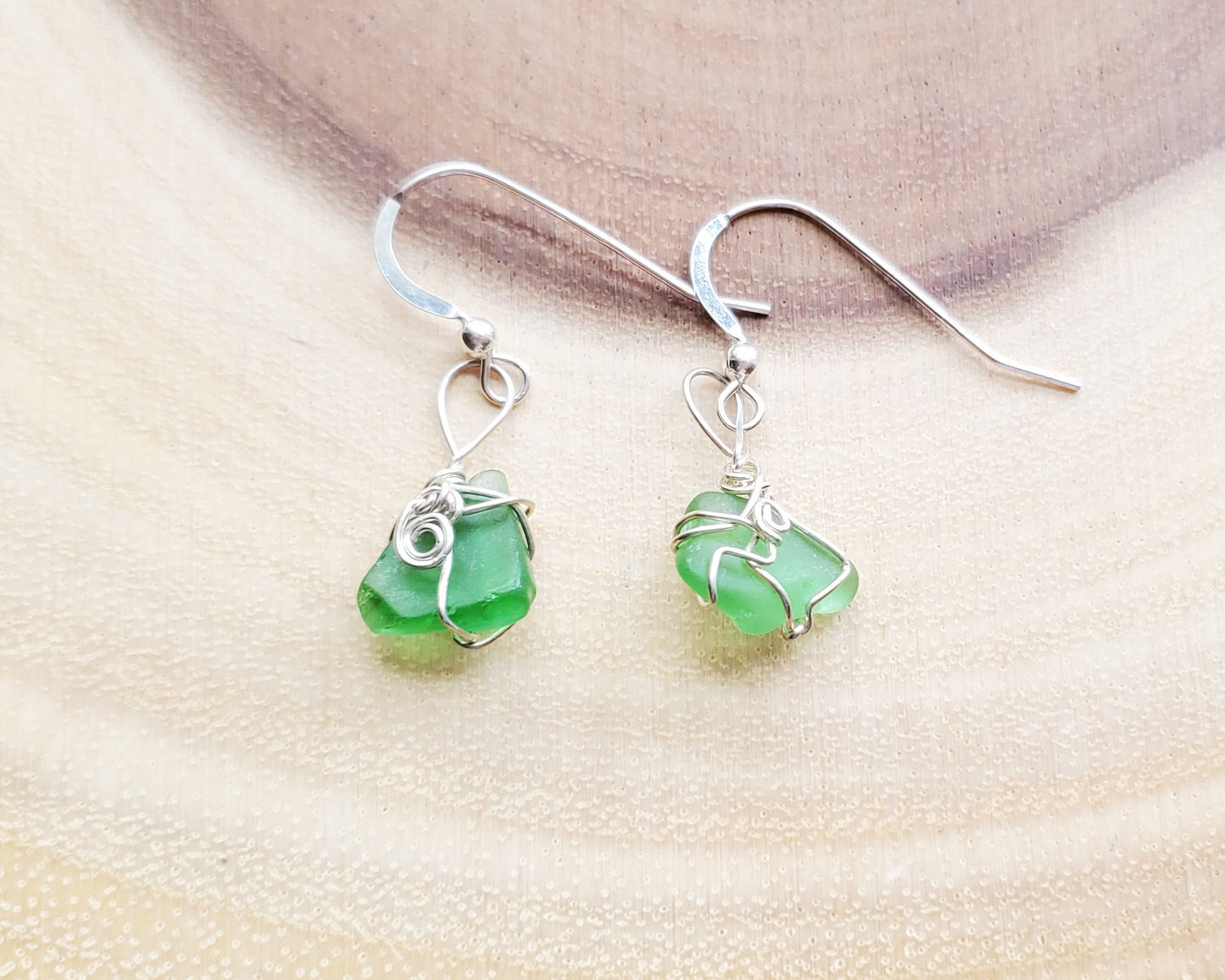 Peaceful Green Sea Glass, Beach Glass Earrings, Sterling Silver Wire Wrapped Green Beach Glass Dangle Earrings displayed on wood