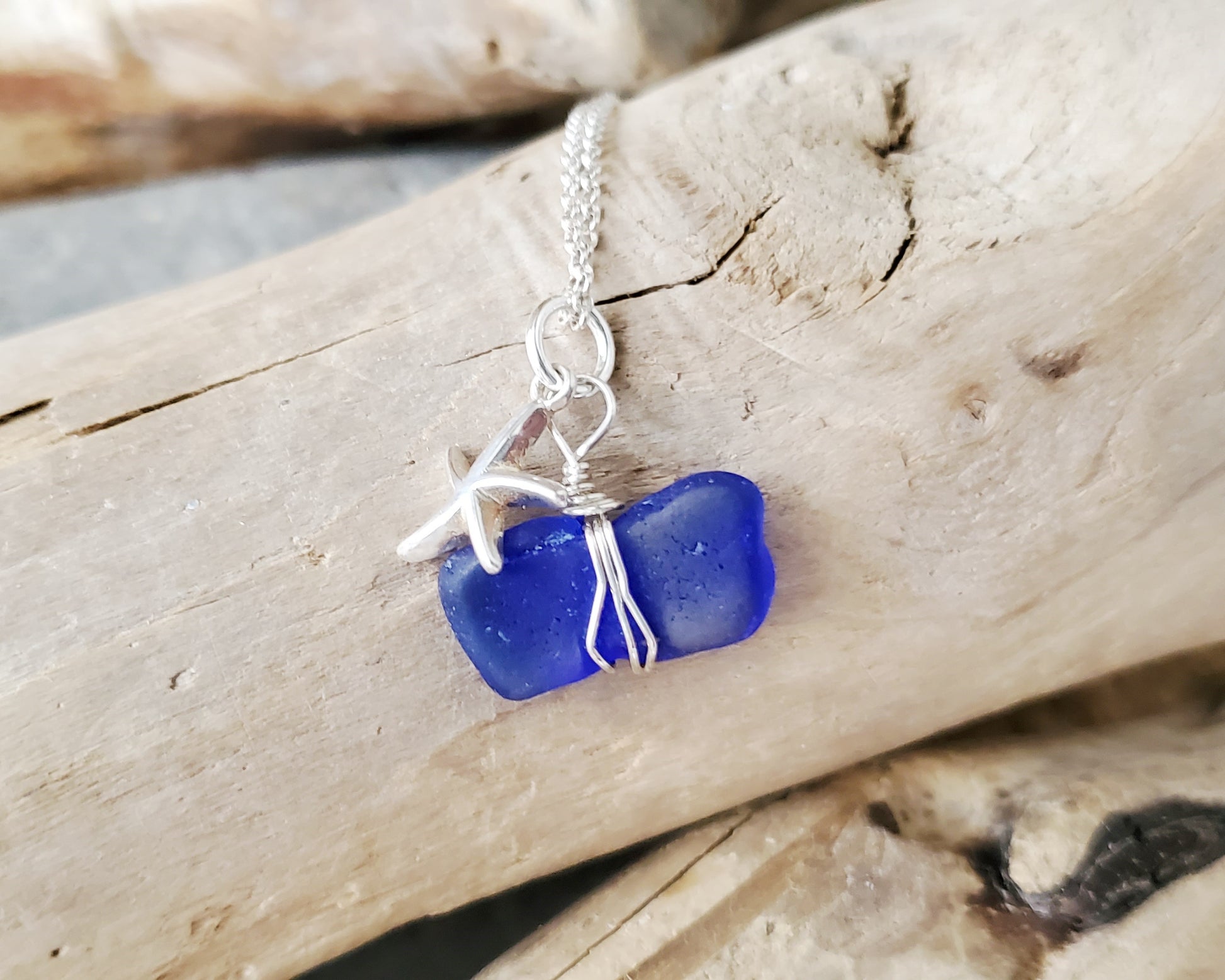 Starfish Blue Beach Glass Pendant Necklace, Sterling Silver with cobalt blue, sapphire blue Beach glass, wire wrapped pendant and starfish on rolo chain. Displayed on beach wood 