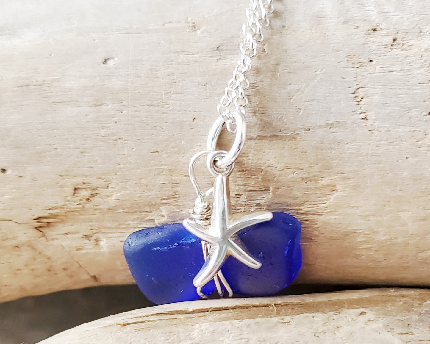 Starfish Blue Beach Glass Pendant Necklace, Sterling Silver with cobalt blue, sapphire blue Beach glass, wire wrapped pendant and starfish on rolo chain. Displayed on beach wood